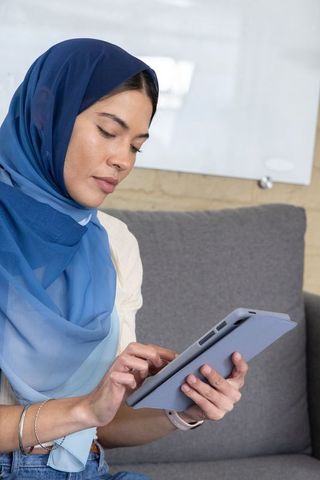 Young woman wearing blue hijab using tablet in modern workspace