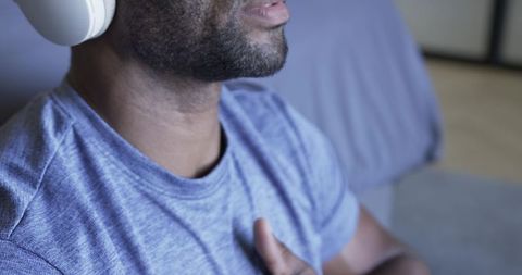 Mature man listening with white headphones, hand on chest, relaxing in bedroom closeup