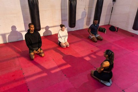 Diverse fitness group kneeling in boxing studio during instructor-led martial arts training
