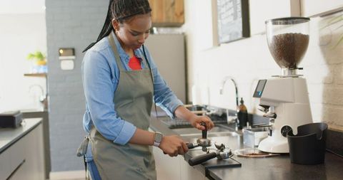 African american barista tamping portafilter preparing espresso behind coffee counter