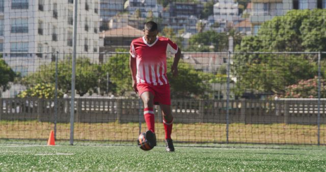 Biracial male football player wearing red uniform training on outdoor pitch. Football, sports and fitness.