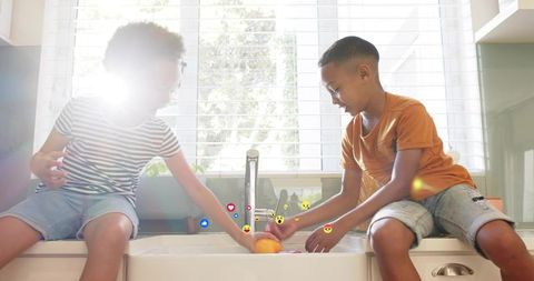 Siblings washing oranges at sunlit farmhouse sink with floating emoji reactions