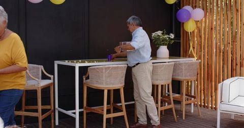 Senior man placing cup at outdoor bar during family backyard celebration