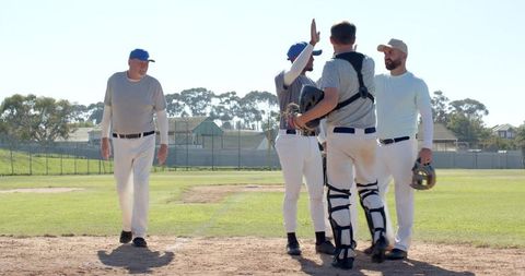 Diverse baseball teammates gathering and high-fiving at home plate on sunny local field