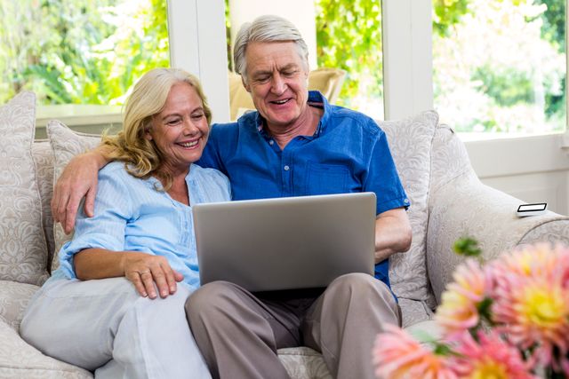 Happy senior couple using laptop while sitting on sofa in living room at home