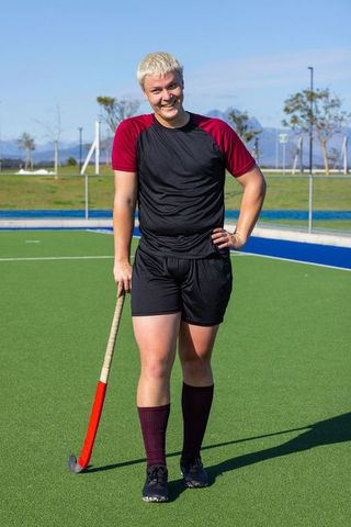 Male field hockey player standing smiling on outdoor turf field