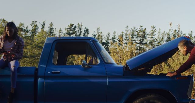 Young friends enjoy an adventurous road trip and repair a classic truck outdoors. Perfect for visuals related to travel, outdoor activities, friendship, teamwork, and vehicle maintenance themes.