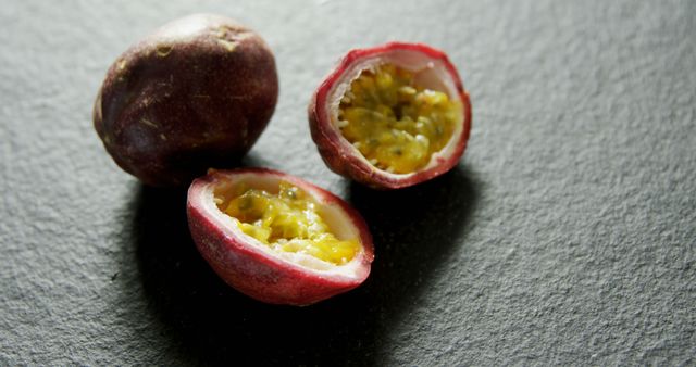 This image features a close-up of fresh passion fruit cut open to reveal its juicy interior with seeds, placed on a dark surface creating a striking contrast. Ideal for use in food blogs, healthy eating brochures, tropical fruit promotions, and culinary websites.