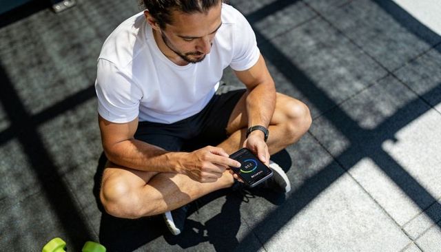 Crosslegged man checking fitness app on smartphone with smartwatch after workout session