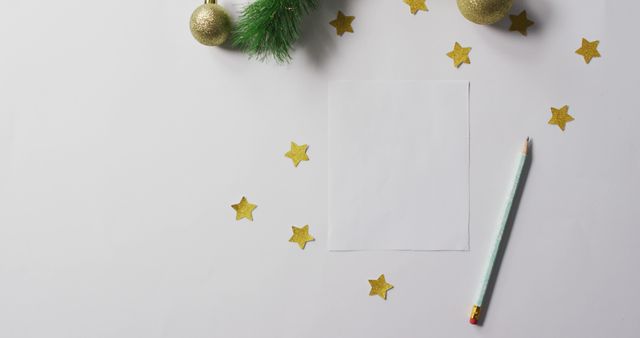 Festive Christmas-themed stationery layout featuring a blank sheet of paper surrounded by gold ornaments, stars, and a pencil. Ideal for holiday greeting card templates, festive invitations, Christmas letters, or holiday event promotions.