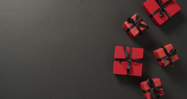 Red gift boxes with black ribbons on black background with copy space. Luxury treat, present, shopping, black friday sale and retail concept digitally generated image.