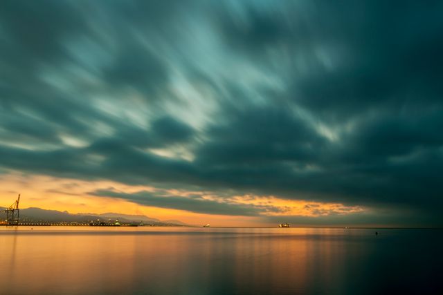 Calming sunrise scene over a serene sea with fascinating long exposure clouds. Great for backgrounds, travel blogs, relaxation themes, meditation visuals, industrial environments, and photography portfolios.