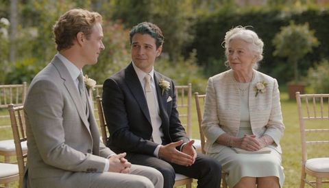 Man in dark suit gesturing while talking with guest and elderly woman at garden wedding