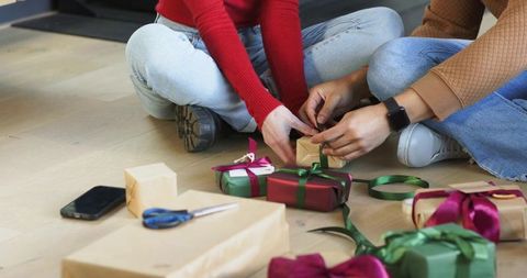 Couple wrapping holiday gifts on hardwood floor cozy casual ribbons boxes present