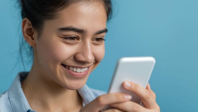 Smiling Woman Engaging with Smartphone Against Blue Wall