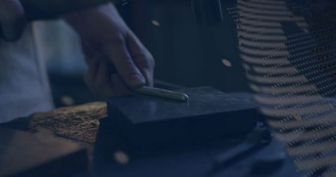 Blacksmith sharpening steel blade on whetstone at workshop bench, closeup craftsmanship