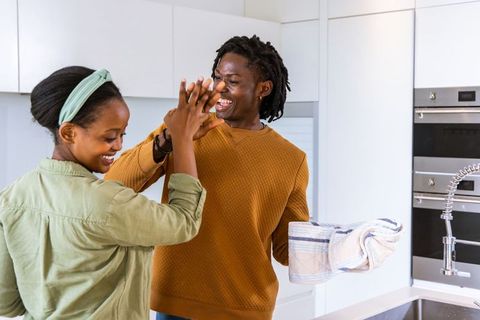 African american couple high-fiving in bright modern kitchen while drying dishes