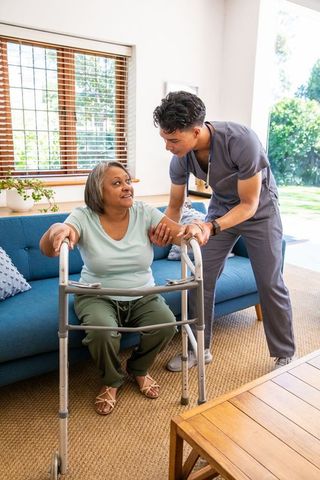 Hispanic caregiver assisting senior woman with walker in living room