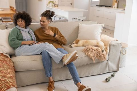 Young couple relaxing on neutral sofa with sleeping puppy in modern open-plan living space