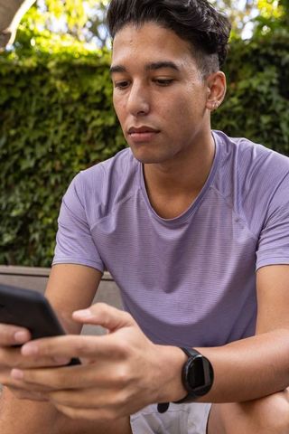 Young adult relaxing outdoors checking smartphone and fitness watch
