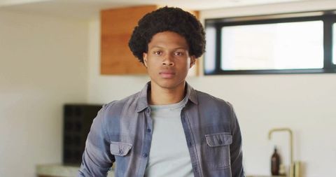 Standing young man in modern sunlit kitchen wearing gray shirt and light tee