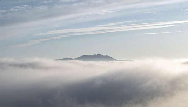 Misty Mountain Ridge Rising Above Sea of Fog Under Cirrus-Streaked Sky for Serene Panorama
