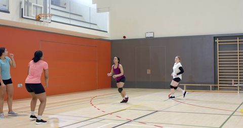 Female volleyball players practicing indoor team drill on gym court wearing knee pads