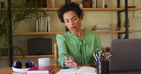 Focused Woman Writing at Cozy Home Office Desk with Laptop and Pen