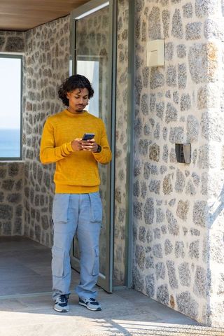Asian man standing in modern stone entryway holding smartphone with ocean view