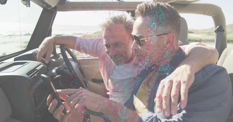Mature friends sharing smartphone while driving convertible on sunny coastal road