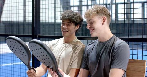 Friends Enjoying Padel Examining Rackets on Blue Court