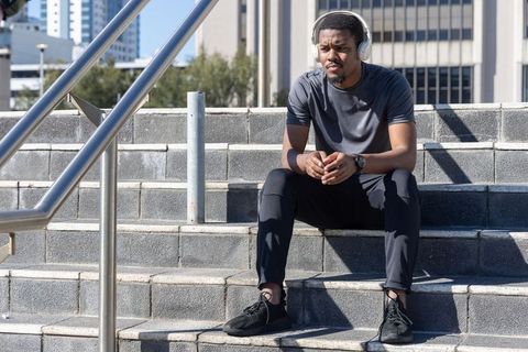 African american man in 20s resting on city steps with headphones and athletic wear