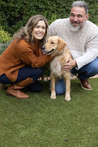 Couple crouching and petting golden retriever on backyard lawn wearing cozy knit sweaters