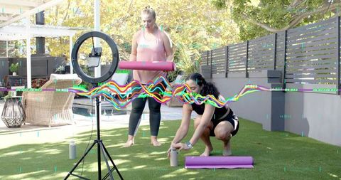 Outdoor fitness coaching guiding client unrolling yoga mat beside ring light for workout
