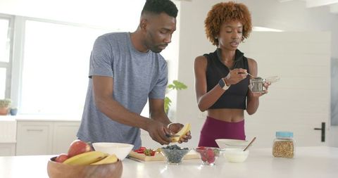 Couple preparing healthy breakfast of fruit, yogurt and granola on bright kitchen island