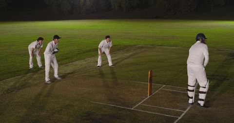 Night cricket fielders waiting in slips while batsman standing at crease under floodlights