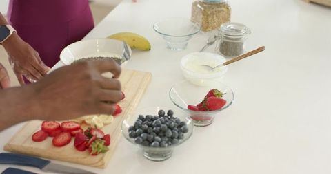 Couple preparing fresh fruit and yogurt breakfast on white kitchen counter with smartwatch