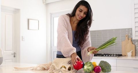 Woman arranging fresh vegetables in reusable bag in kitchen