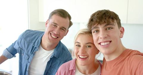 Smiling family taking selfie in bright modern kitchen wearing casual denim and rust outfits
