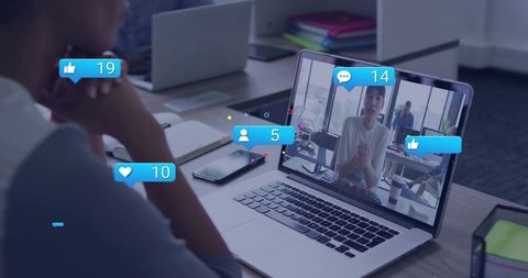 Woman watching remote video call on laptop with social reaction overlays in modern office