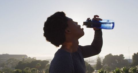 African-american athlete drinking water while exercising outdoors