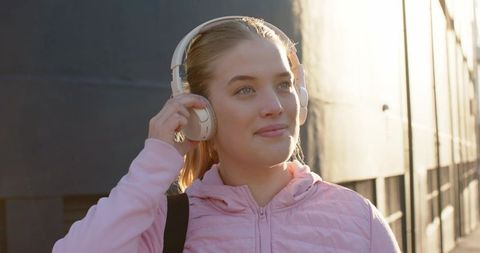 Young woman listening to music with headphones during golden hour in urban alleyway
