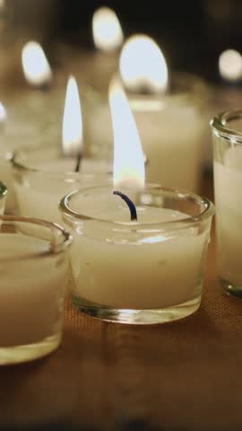 Vertical video of flickering votive candles on wooden table closeup with melting wax and warm bokeh 