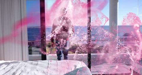 Standing woman facing ocean through glass doors in sunlit bedroom with pink light overlay