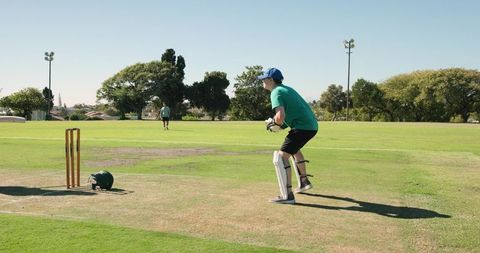 Diverse team wicketkeeper crouching ready to catch on cricket field with stumps, helmet