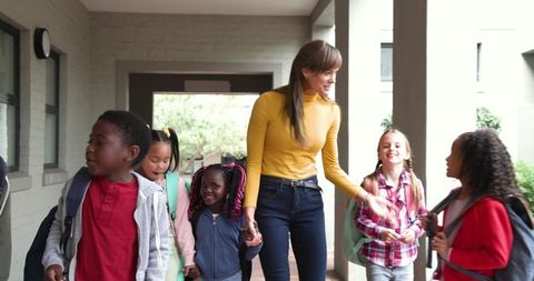 Teacher and Diverse Children Walking School Hallway in Lively Conversation