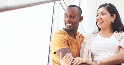 Smiling couple leaning by sunlit window in modern minimalist interior, casual lifestyle