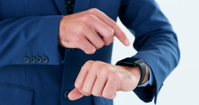 A Caucasian businessman in a blue suit is checking the time on his smartwatch, with copy space. His focus on time management underscores the importance of punctuality in the professional world.