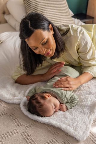 Asian mother bonding with newborn daughter sleeping on cozy blanket, tender nurturing