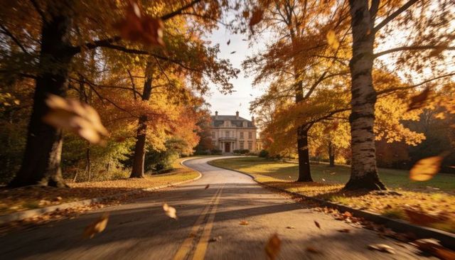 Autumn driveway leading to stately manor with falling leaves, golden trees, winding road